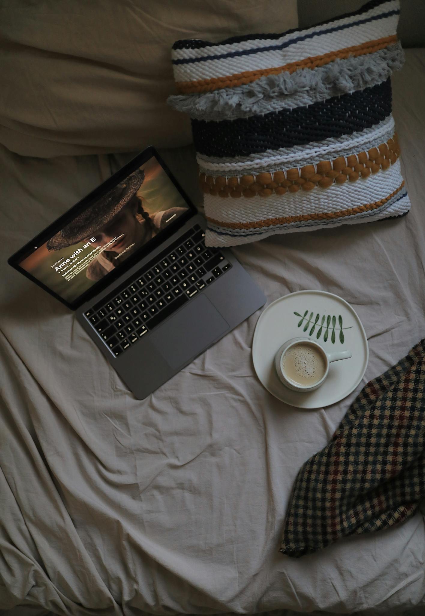 Discover a cozy bed setup with a laptop, coffee, and pillow for ultimate relaxation.